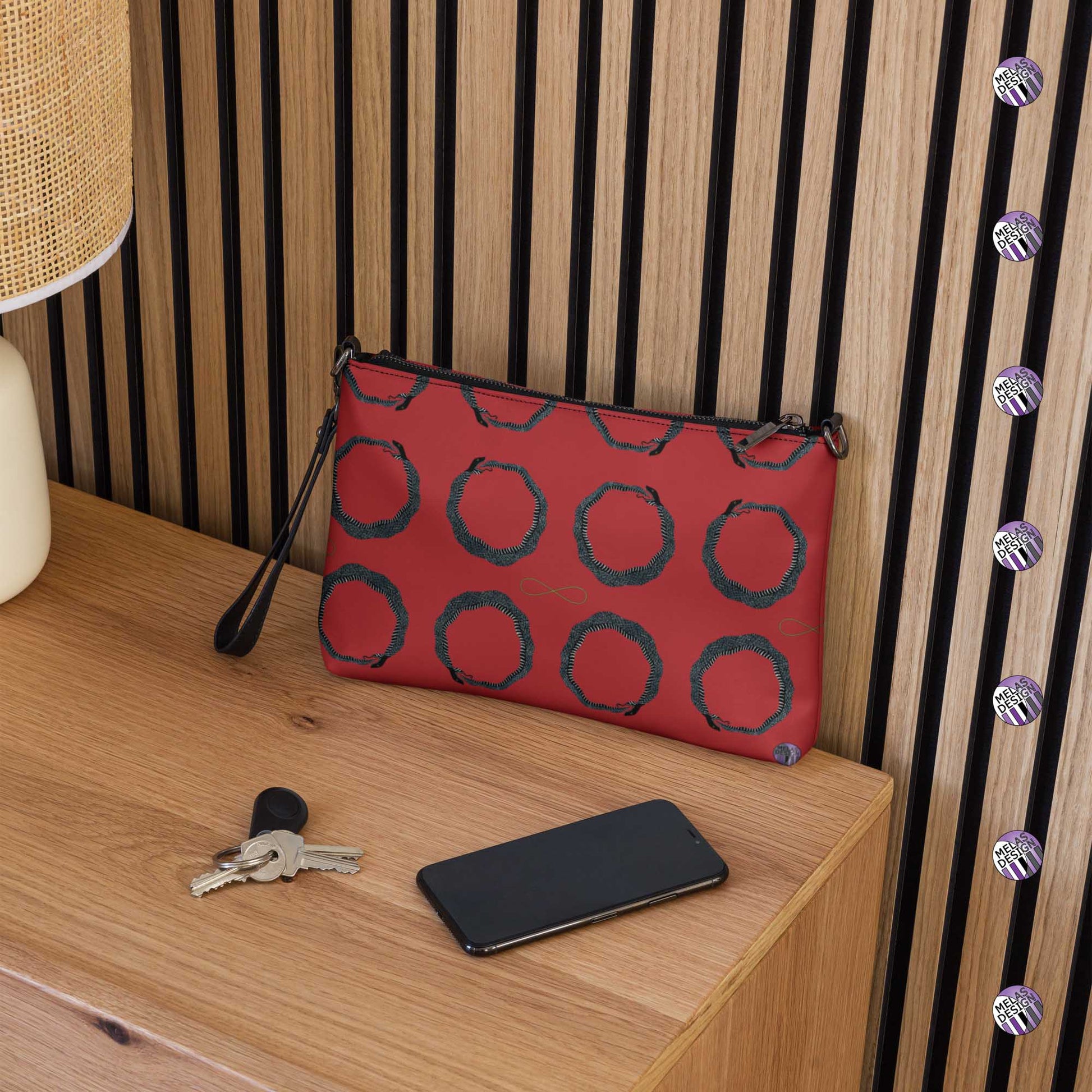 Ouroboros Infinity Cross-Body Bag Red Black; Product mockup on side table with phone and keys; Melasdesign logos