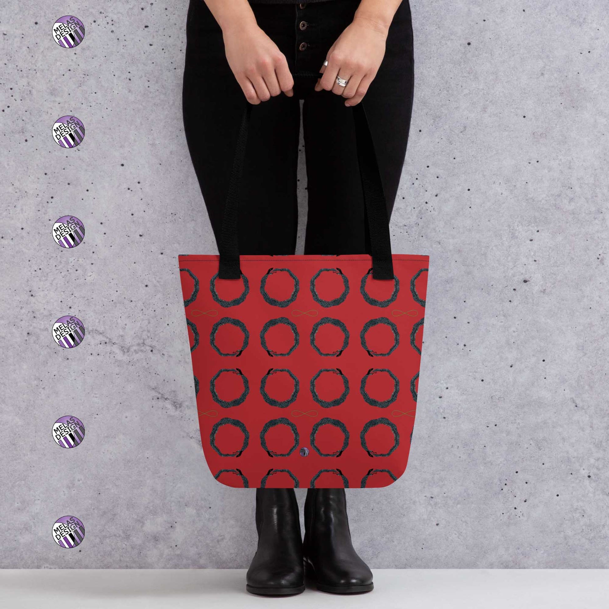 Ouroboros Infinity Pattern Tote Bag Red Black; mock-up with model holding tote in front standing by gray wall with Melasdesign logos